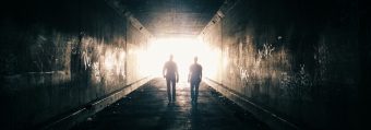 Two men walking toward light, silouhetted, in a tunnel.
