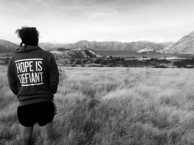 Girl looking at a mountain range with Hope is Defiant on her sweatshirt.