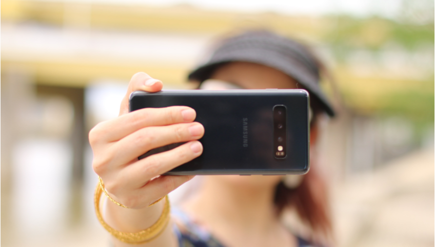 Woman holding a camera front and center while she takes a selfie.