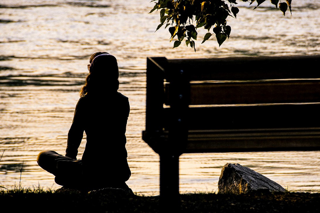 Silhouette of a woman looking over a pond with headphones on.