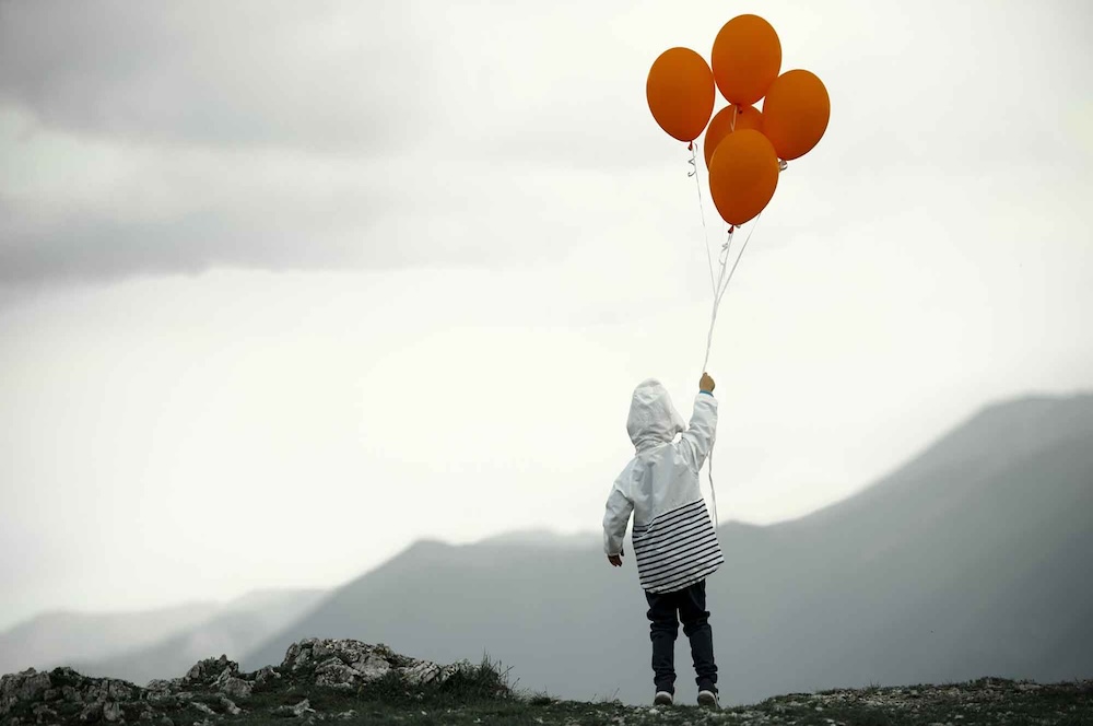 Boy holding onto helium balloons.